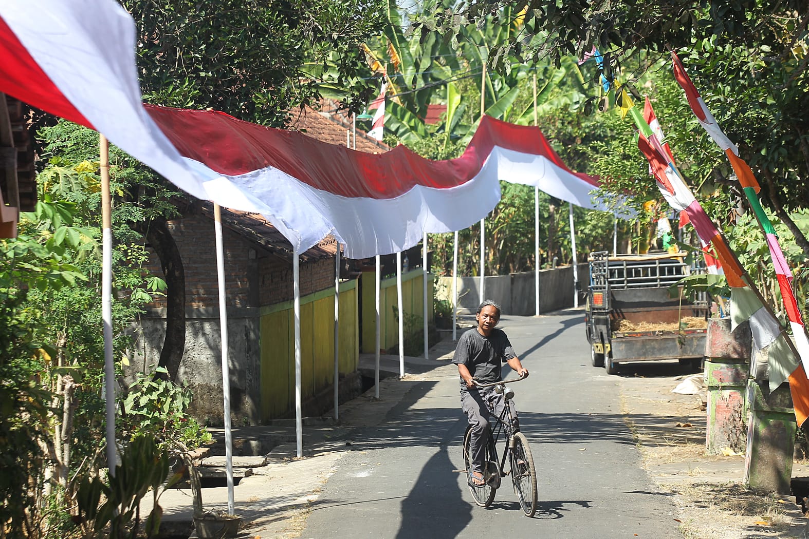 MERAH PUTIH: Warga menaiki sepeda di dekat bendera Merah-Putih di Dusun Karang, Kelurahan Jatisarono, Kapanewon Nanggulan, Kulon Progo, DIY, Selasa (1/8). (Guntur Aga Tirtana/Radar Jogja)