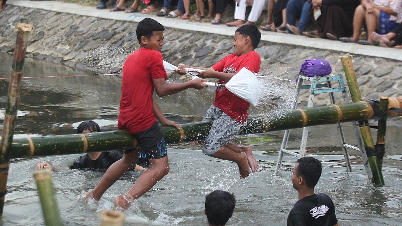 PITULASAN: Dua anak sedang mengikuti lomba gebuk bantal di Selokan Mataram Dusun Mayangan, Trihanggo, Kapanewon Gamping, Sleman, Minggu (6/8). (Guntur Aga Tirtana/Radar Jogja)