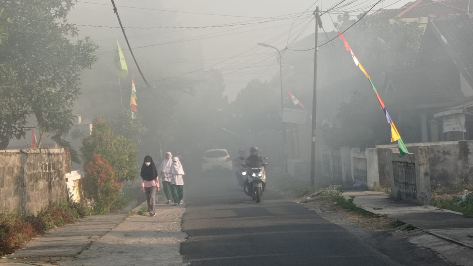 POLUSI UDARA: Tiga orang siswa berjalan di Jalan Cantel Baru, Muja Muju Umbulharjo, melewati kepulan asap akibat aktivitas bakar sampah di Lapangan Kenari, Selasa (8/8).