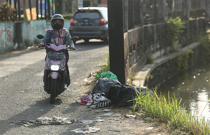 BERSERAKAN: Pengendara melintas di samping tumpukan sampah di pinggir Selokan Mataram, Santren, Caturtunggal, Depok kemarin (14/8).
