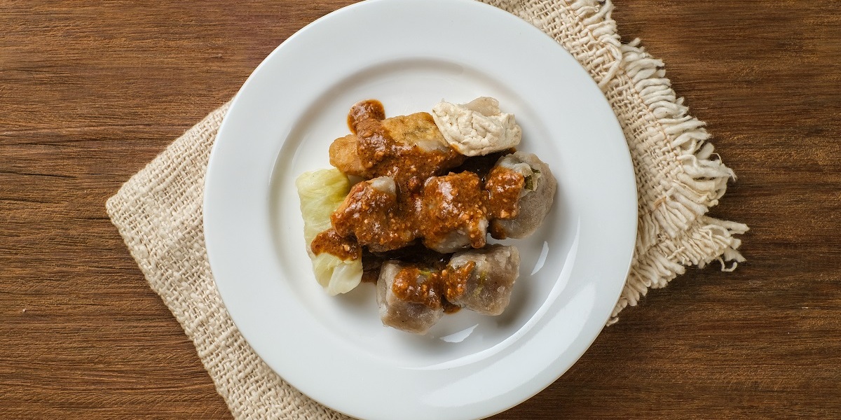 Siomay Bandung or steamed dumplings,  Indonesian traditional street food with spicy peanut sauce and soy sauce served on a white plate.