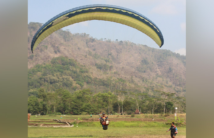 POTENSI: Pj Bupati Kulon Progo Ni Made Dwipanti Indrayanti mendarat dengan selamat usai terbang tandem paralayang (kanan) saat gelaran Festival Paralayang di Bukit Girisembung, Minggu (8/10).ISTIMEWA