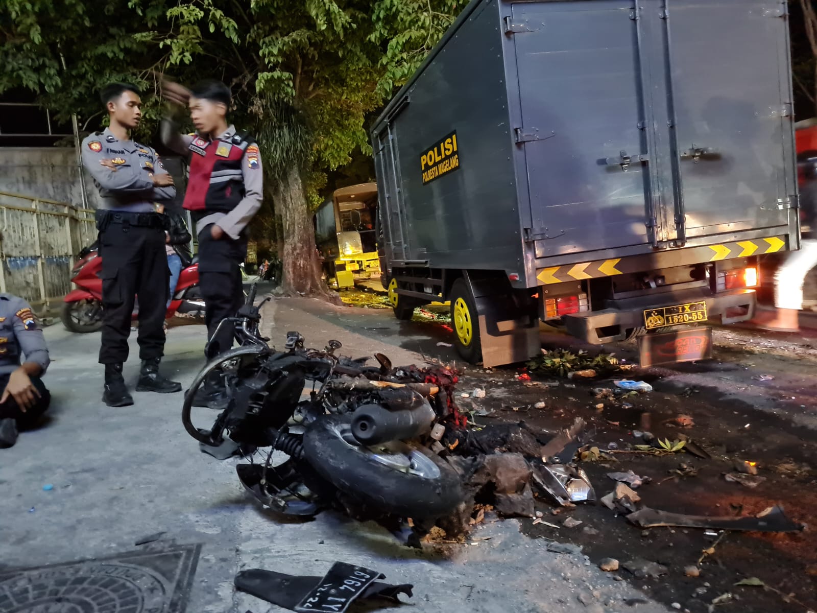 Polisi berjaga di depan rongsokan motor yang dibakar massa di kawasan Muntilan, Magelang Minggu (15/10)