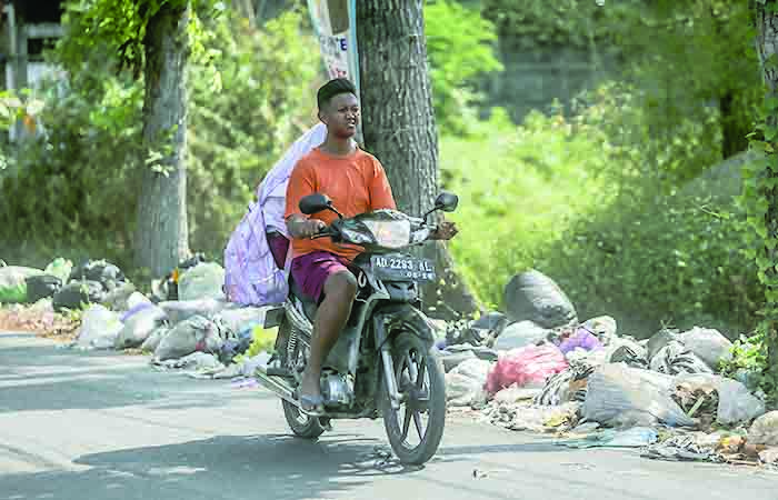 TAK SESUAI: Pengandara motor melintasi sampah yang menumpuk di Jalan Kabupaten, Trihanggo kemarin (16/10). Sampah sudah menumpuk lebih dari sepekan dan menimbulkan