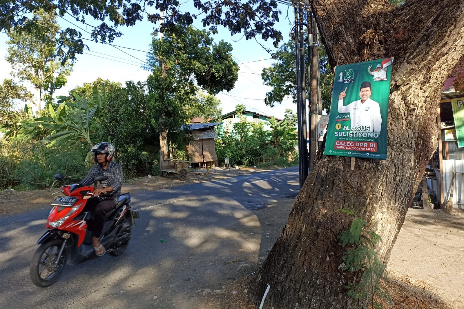 DI POHON: Pengendara melintas di samping alat peraga sosialisasi (APS) yang terpasang di pohon di Jalan Tembi, Kalurahan Timbulharjo, Sewon, Bantul, Minggu (19/11). (Gregorius Bramantyo/Radar Jogja)