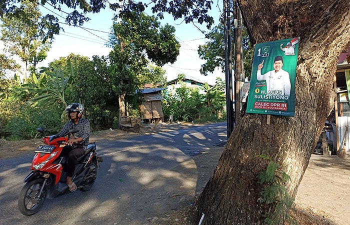 TIDAK SESUAI: Pengendara melintas di samping alat peraga sosialisasi (APS) yang terpasang di pohon di Jalan Tembi, Kalurahan Timbulharjo, Sewon Minggu (19/11).GREGORIUS BRAMANTYO/RADAR JOGJA&nbsp;