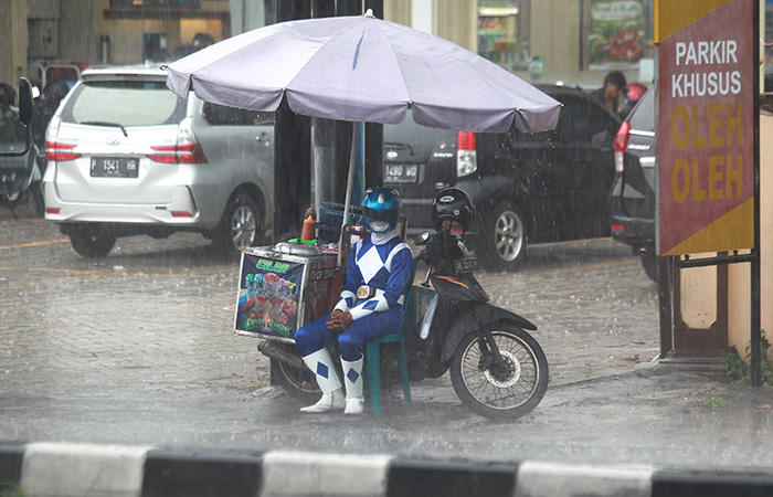 NGEYUP: Penjual jajanan berkostum Power Ranger berteduh saat hujan mengguyur Jalan Magelang, kawasan Triharjo,  Sleman, Rabu (29/11).