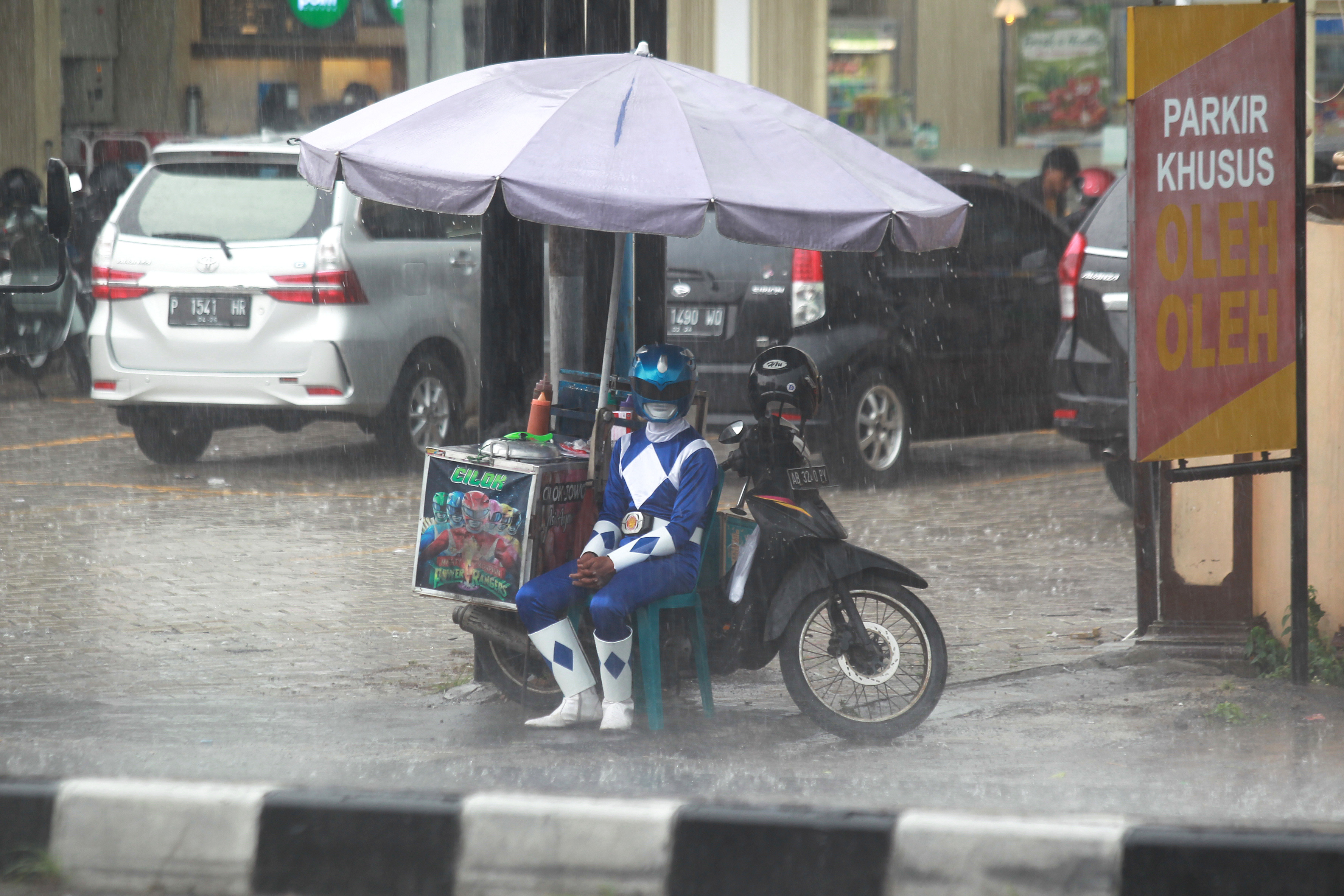 Penjual jajanan berkostum Power Ranger berteduh saat hujan mengguyur Jalan Magelang, Sleman, Rabu (29/11). Memasuki musim penghujan, Badan Penanggulangan Bencana Daerah (BPBD) DIJ mengimbau masyarakat