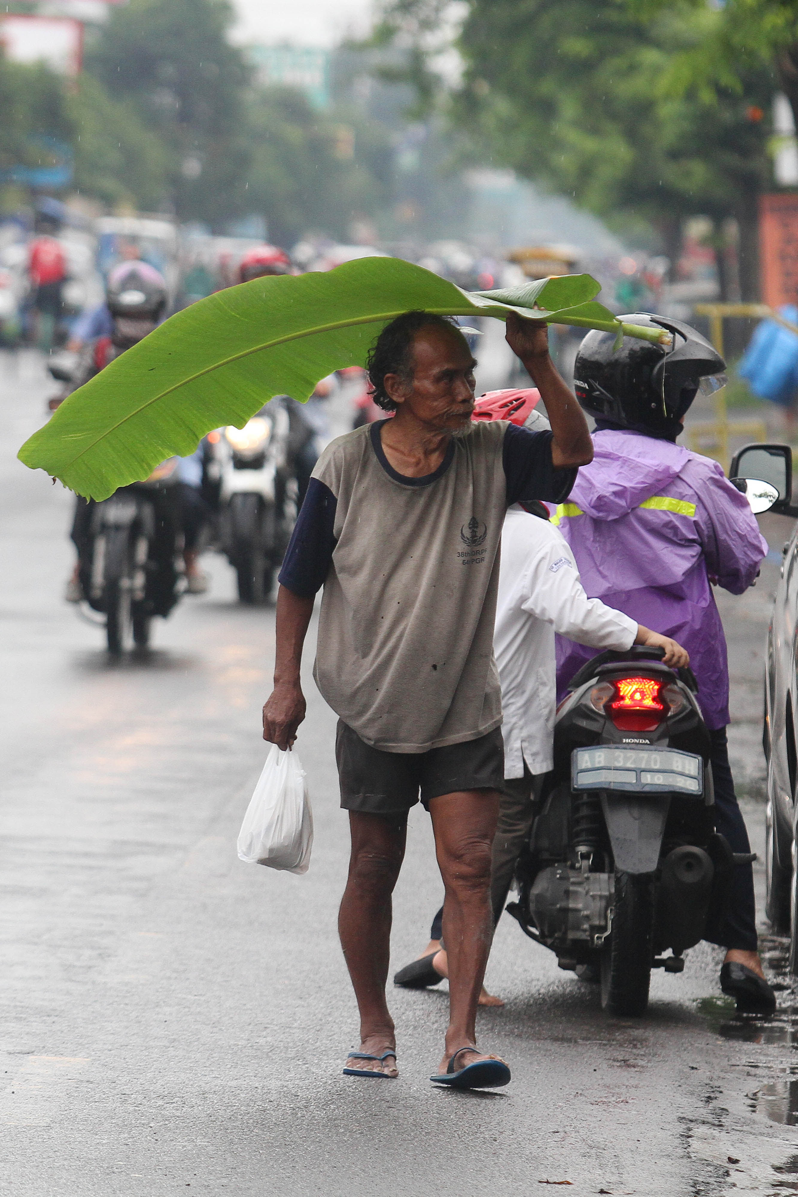 Pejalan kaki menggunakan daun pisang sebagai payung saat hujan mengguyur Kota Jogja.