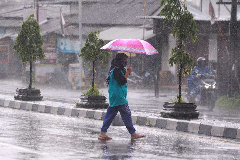 DERAS: Warga memakai payung untuk menghindari air hujan saat menyebarang jalan raya.
