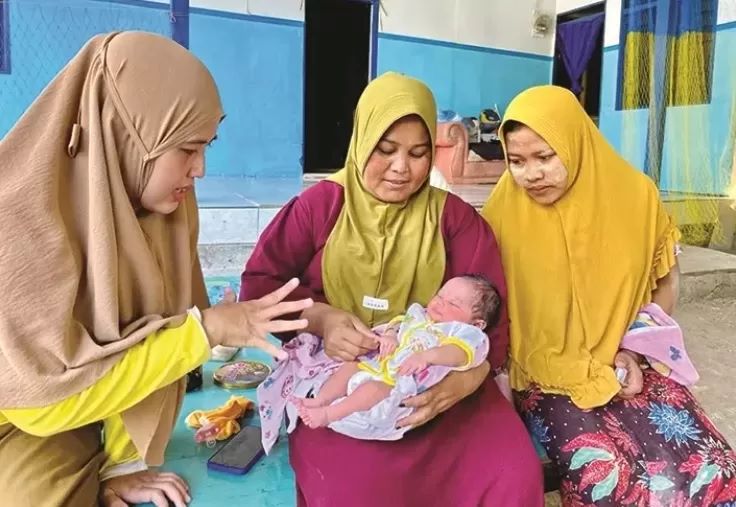 Bidan Desa Sejati Yuliani (kiri) menghibur Amira Hilyatun Nisak yang digendong dukun bayi Halisa di samping Subaidah (kanan) Selasa (30/1). (ANIS BILLAH/JPRM)
