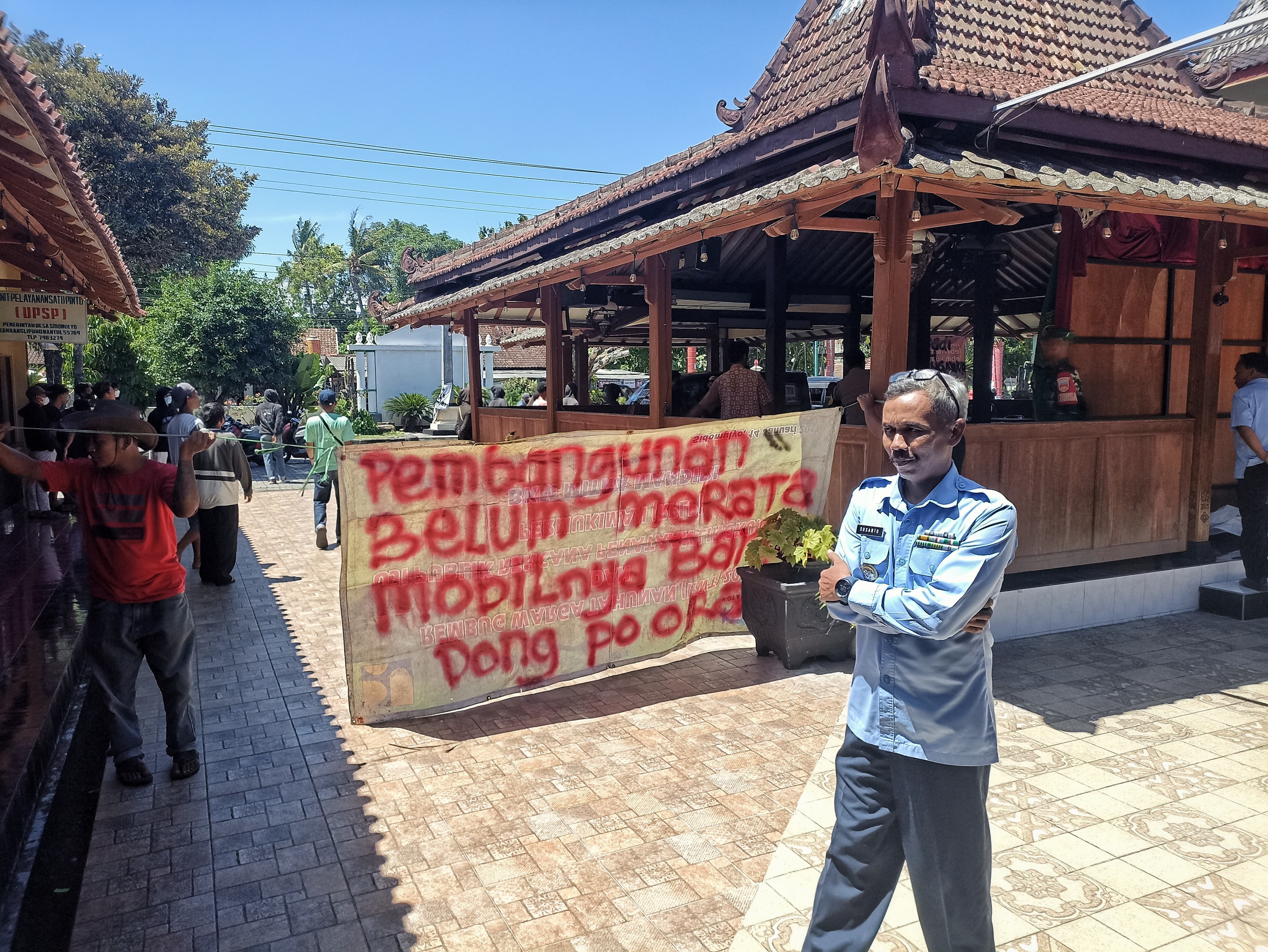 PROTES: Warga membentangkan spanduk di hadapan Lurah Sidomulyo saat aksi unjuk rasa di Kantor Kalurahan Sidomulyo, Bambanglipuro, Bantul, Selasa (19/3).