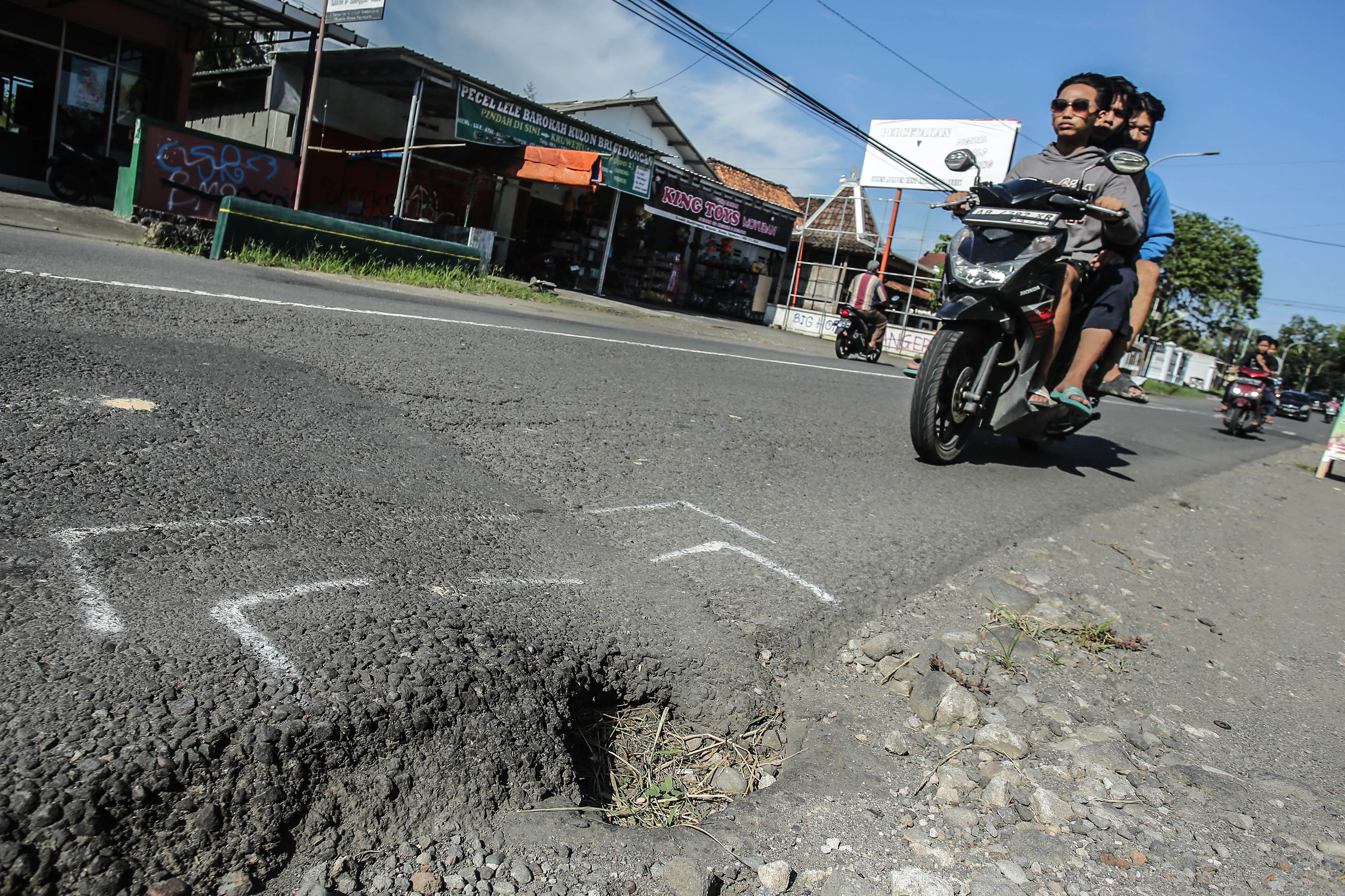 HATI-HATI: Pengendara motor melintas disamping lubang di jalan Ngapak-Kentheng, Sumberagung, Moyudan, Sleman, Senin (18/3).