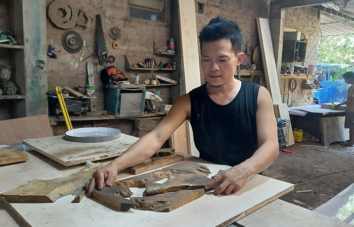 KREATIF: Dwi Nuryanto saat berkarya dan sejumlah hasil karya yang masih dalam pembuatan. Ia memanfatkan kayu krowak untuk menuangkan ide seninya.