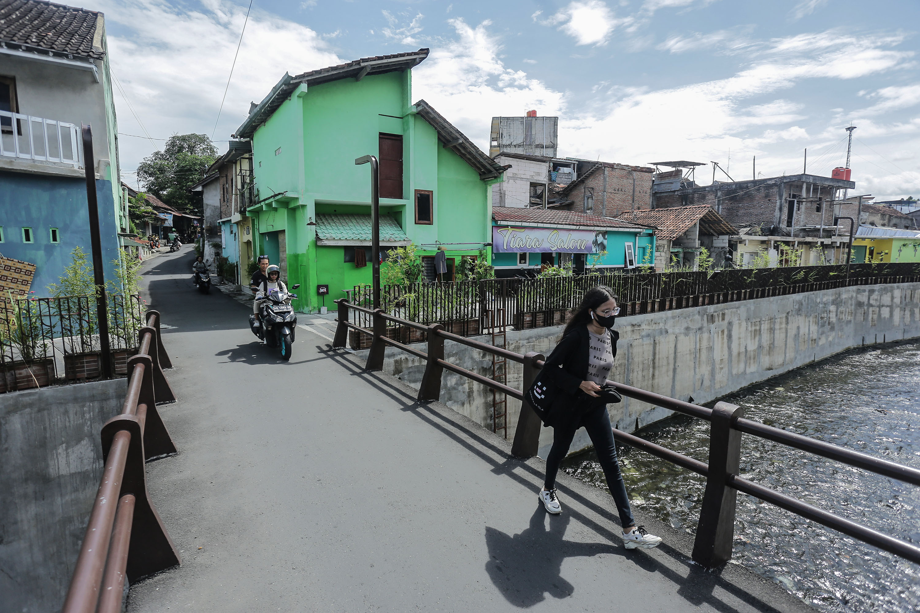 warga melintasi jembatan berlatar rumah padat penduduk di kawasan Pringgondani, Caturtunggal, Depok, Sleman, rabu (17/4). Pertumbuhan jumlah penduduk di Sleman tiap tahun terus terjadi. Disdukcapil Sleman mencatat di awal tahun 2024 ada 6000 orang masuk (
