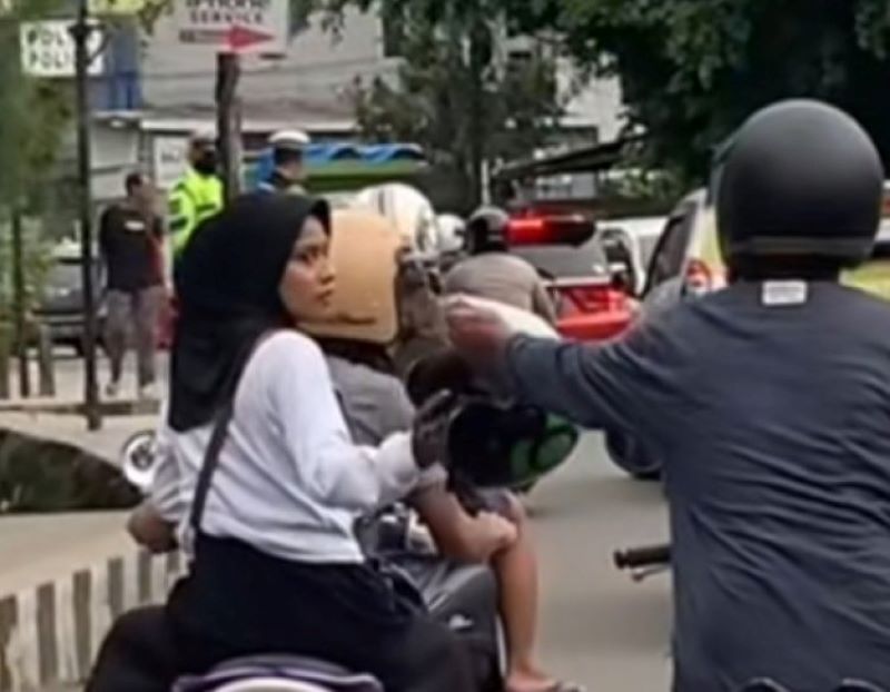Seorang driver ojol meminjamkan helm kepada pengendara lain saat ada razia polisi di jalanan.