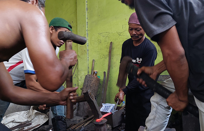 Pandai besi bergiliran menempa bahan yang telah dipanaskan.
