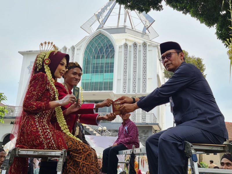 SEMRINGAH: Pasangan pengantin ini memperlihatkan buku nikah di atas tangga di depan Masjid Manaarul
