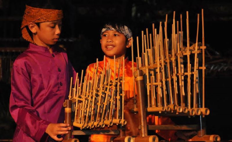 Dua orang anak yang sedang memainkan alat musik angklung.