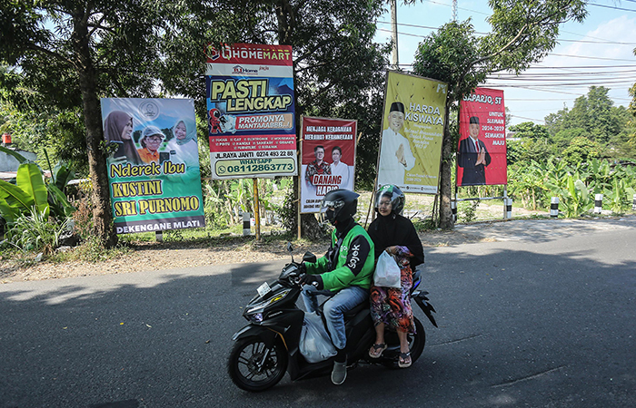 Pengendara motor melintas disamping deretan spanduk pilkada dengan wajah tokoh Sleman di kawasan Sumberadi, Mlati, Sleman, Senin (22/7).