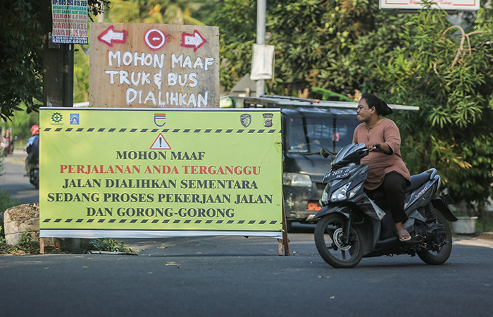 PENANDA: Pengendara motor melintas di samping papan pemberitahuan perbaikan jalan di kawasan Babadan, Wedomartani, Sleman (5/8).