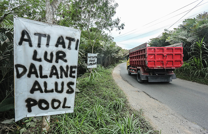 BENTUK PROTES: Warga melintasi spanduk protes jalan rusak dan berdebu akibat sering dijadikan jalur untuk truk pengangkut pasir di Kawasan Wonokerto, Turi, Sleman Senin (26/8).