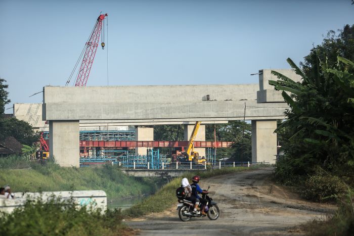 BELUM BERES: Warga melintas berlatar proyek pembangunan jalan tol Jogja-Bawen di kawasan Margokaton, Sayegan, Sleman Kamis (5/9/2024). Saat ini masih ada 26 bidang tanah belum dibebaskan