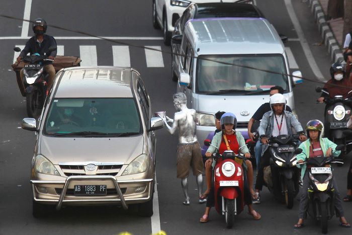 Manusia silver saat meminta uang kepada pengendara mobil yang sedang berhenti menunggu lampu APILL.