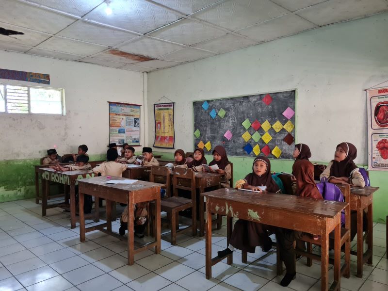 KURANG LAYAK: Para siswa saat kegiatan belajar mengajar di MI Sirojul Munir dengan kondisi atap ruang kelas yang bocor.