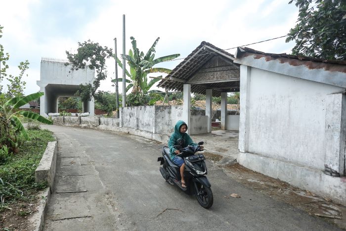 BELUM DIRELOKASI: Warga melintas di depan makam Si Jambu dengan latar konstruksi jalan tol di kawasan Margokaton, Seyegan, Sleman Kamis (26/9/2024).