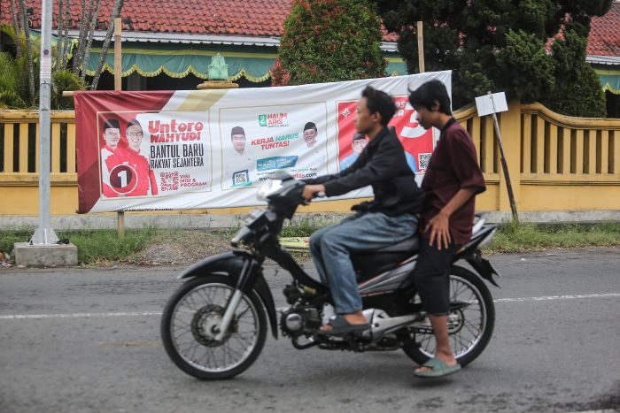 Pengendara motor melintasi spanduk tiga pasangan calon pilkada Bantul di kawasan Tirtonirmolo, Kasihan, Bantul, Sabtu (2/11/2024).