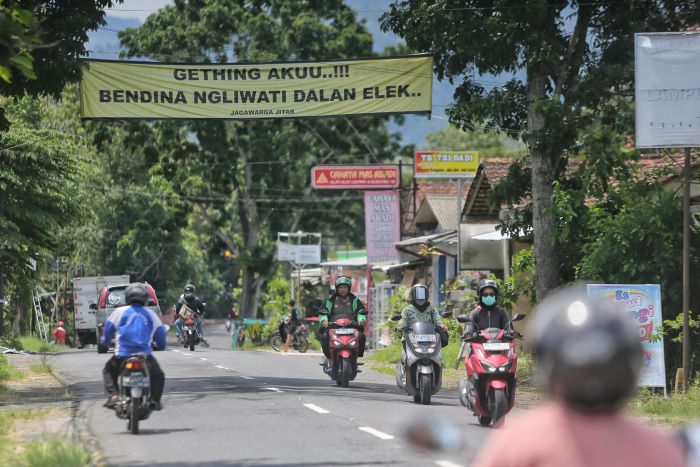 BENTUK PROTES: Pengendara motor melintasi spanduk yang berisikan keresahan warga soal rusak Jalan Ngapak-Kentheng kawasan Minggir, Sleman Selasa (3/12/2024).