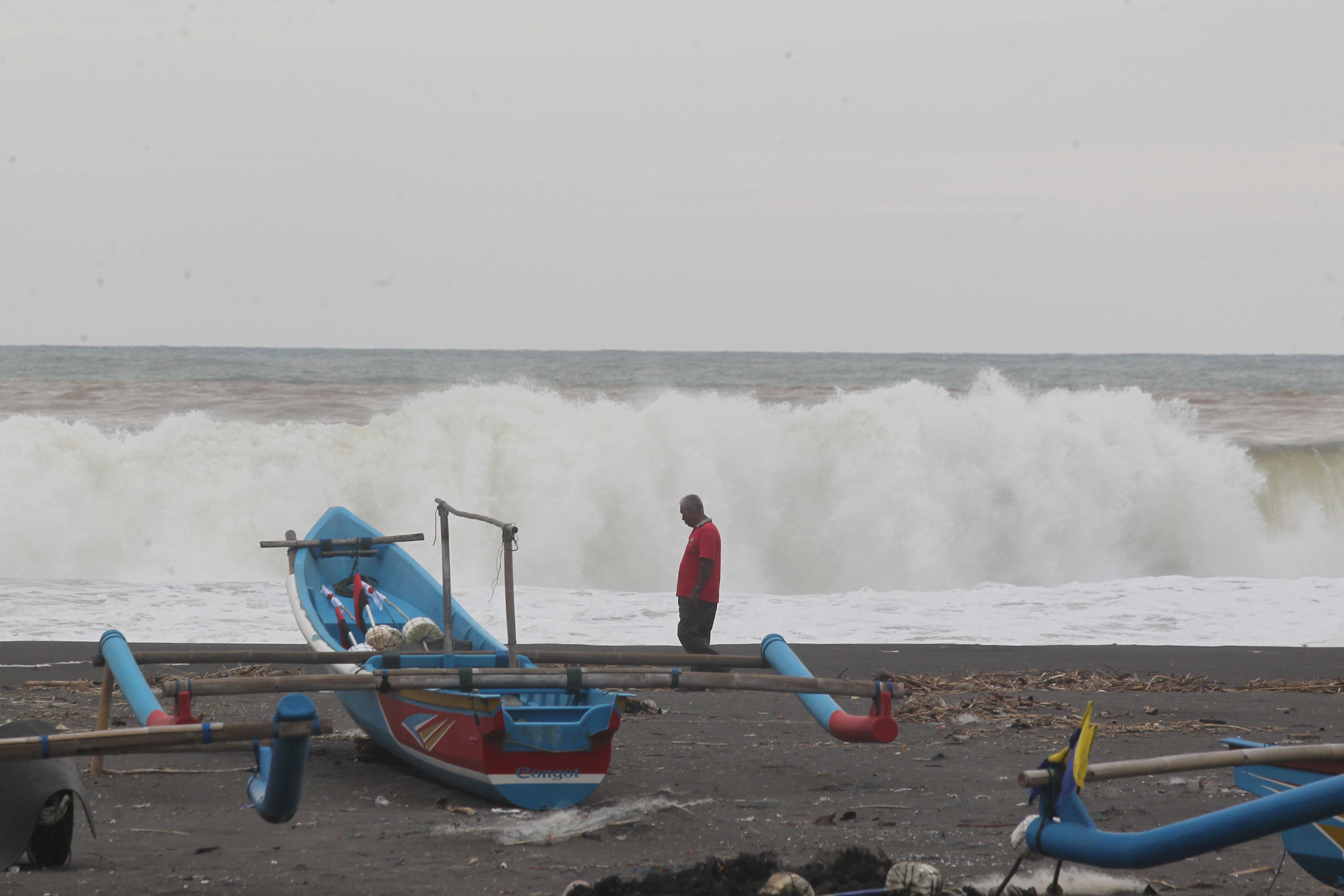 Warga melintas di dekat perahu nelayan yang bersandar di Pantai Congot, Kulon Progo, kemarin (12/12). Belasan nelayan setempat memilih menyandarkan perahu dan tidak melaut karena gelombang tinggi