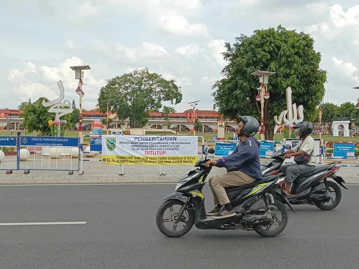 DITUTUP SEMENTARA : Pengendara motor melintas di depan plang barikade yang menutup pintu area parkir Alun-alun Pancasila.