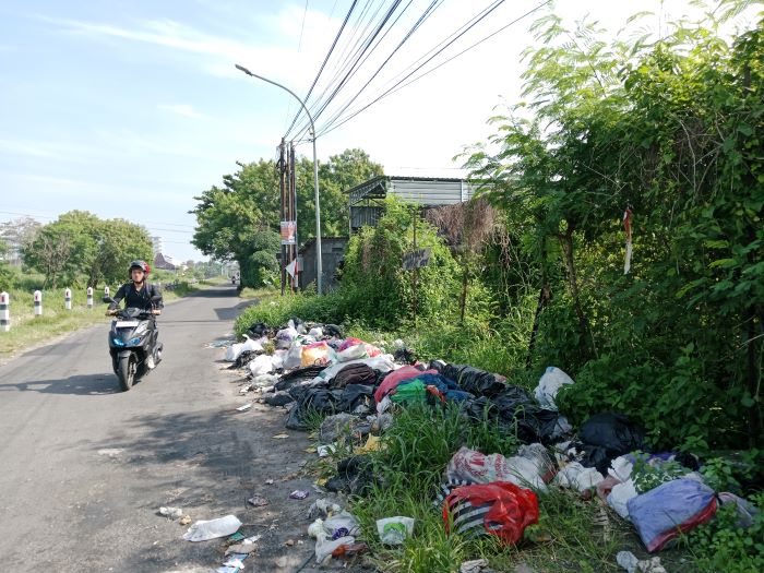 BERSERAKAN: Pengendara sepeda motor saat melewati tumpukan sampah liar yang dibuang di samping Selokan Mataram Selasa (11/2).