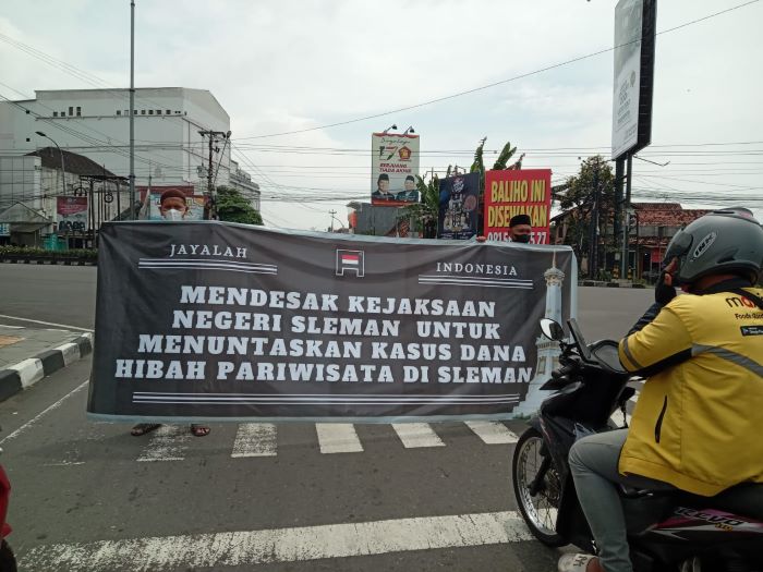 TURUN KE JALAN: Aliansi Rakyat Peduli Indonesia (ARPI) saat membentangkan spanduk soal kasus dana hibah pariwisata di simpang empat Denggung, Sleman Rabu (19/2).