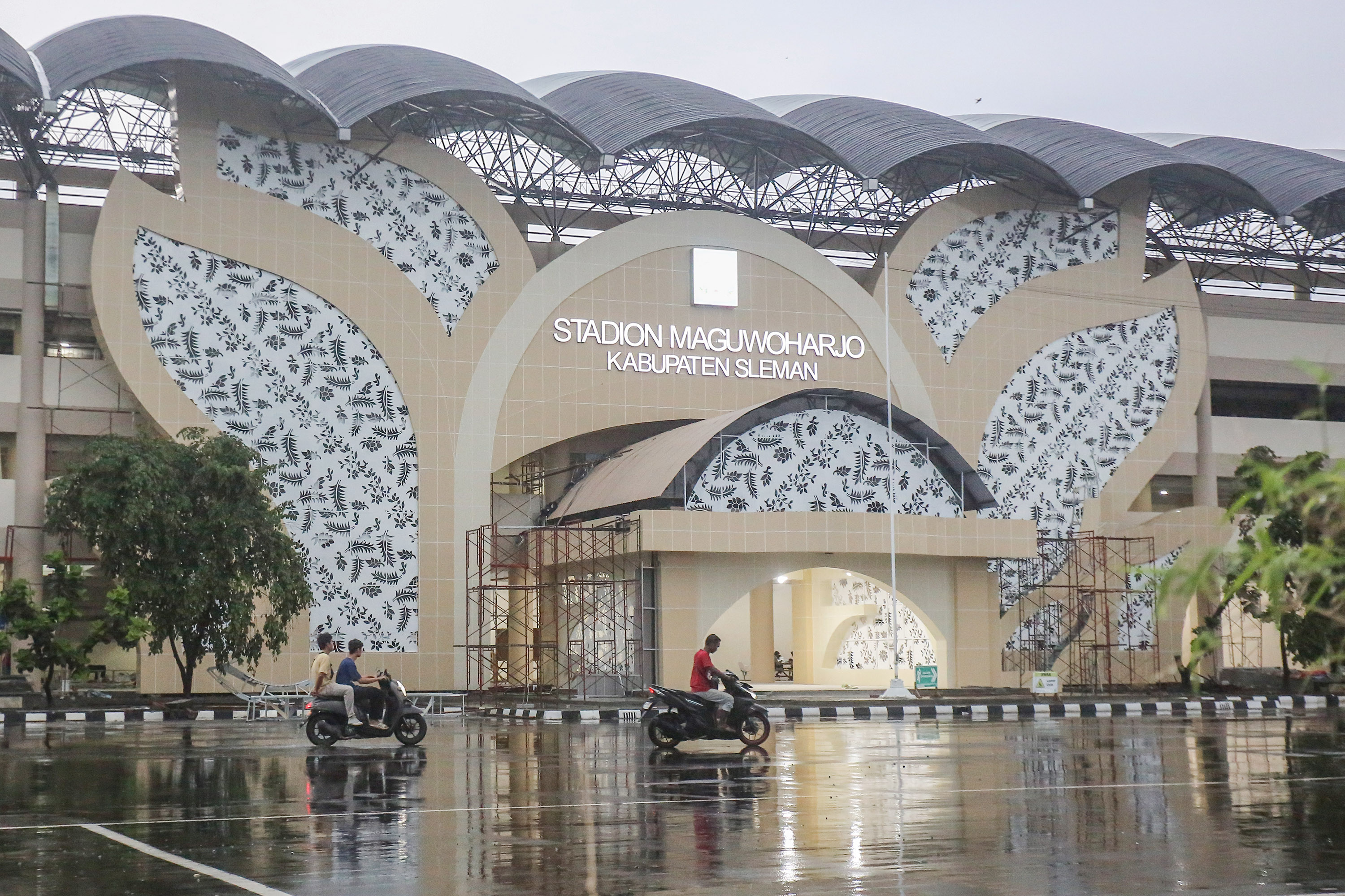 Pekerja melintas usai hujan saat sore hari di depan stadion Maguwoharjo, yang menggunakan ornamen batik Sinom Parijotho
