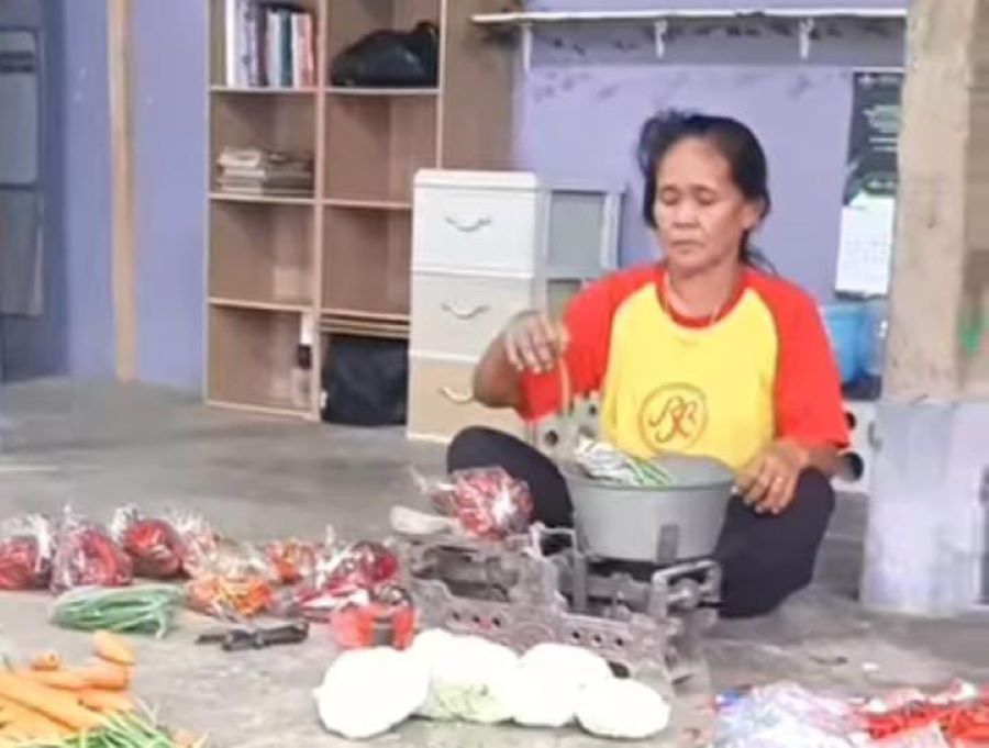 Seorang pedagang sedang melayani pembelian sayur di pasar tiban miliknya.