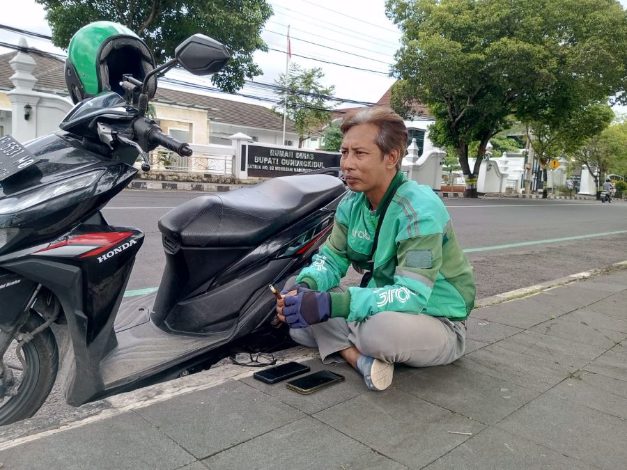 Driver Ojol, Suryo Putro sendang mangkal di Alun-alun Wonosari sembari memantau aplikasi Grabnya.