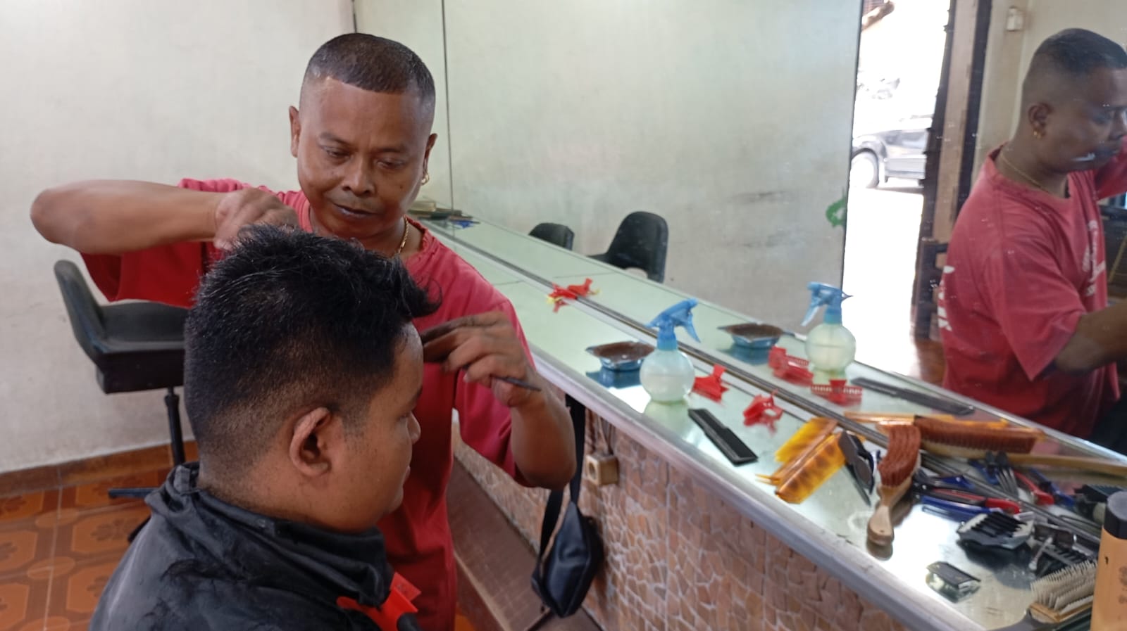 Salah satu karyawan Potong Rambut Dorlen saat memangkas rambut pelanggannya pada Senin (14/7/2025).