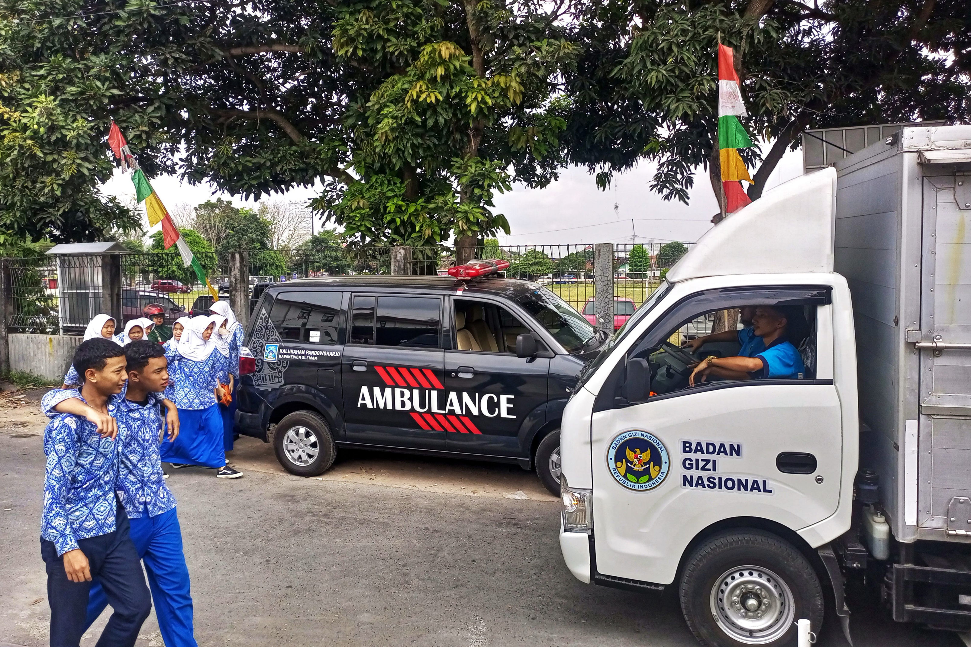 Armada dari dapur Satuan Pelayanan Pemenuhan Gizi (SPPG) Badan Gizi Nasional (BGN) melintas di dekat sejumlah ambulans yang siaga di dekat SMP Muhammadiyah 1 Mlati, Sleman, kemarin (13/8).
