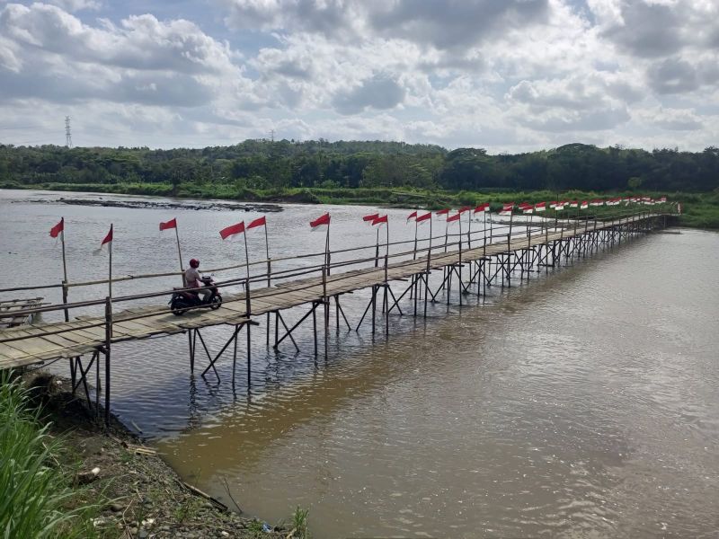 SYAHDU: Pengendara sepeda motor melintas di jembatan sesek Temben yang dihiasi ratusan bendera merah putih, di Ngentakrejo, Kapanewon Lendah, Kulon Progo, Kamis (14/8).