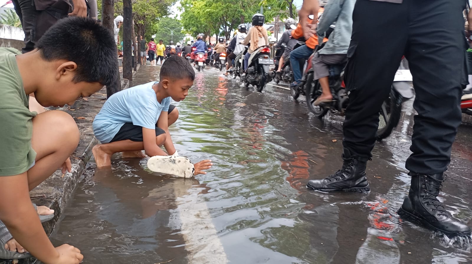 Anak-anak mencari ikan di pinggir Jalan Menteri Supeno yang tergenang akibat meluapnya Sungai Manunggal