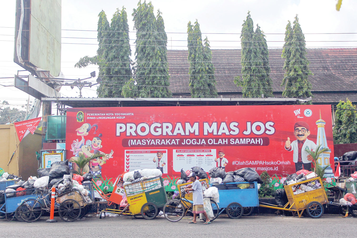 MASIH MENUMPUK: Pengguna jalan melintas di dekat antrean gerobak berisi sampah di depo Purawisata, Jalan Brigjend Katamso, Kota Jogja, (25/8).