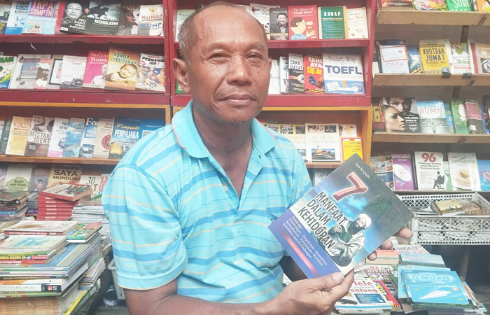 BUAH KETEKUNAN: Fanani sedang memegang buku lawas yang dijualnya Selasa (7/10/2025). (Cintia Yuliani/Radar Jogja)