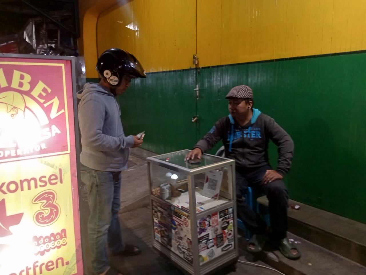 Di emperan Kios depan Pasar Argosari, Wahyu menggelar lapak Samben Bakoel Pulsa setiap malamnya.