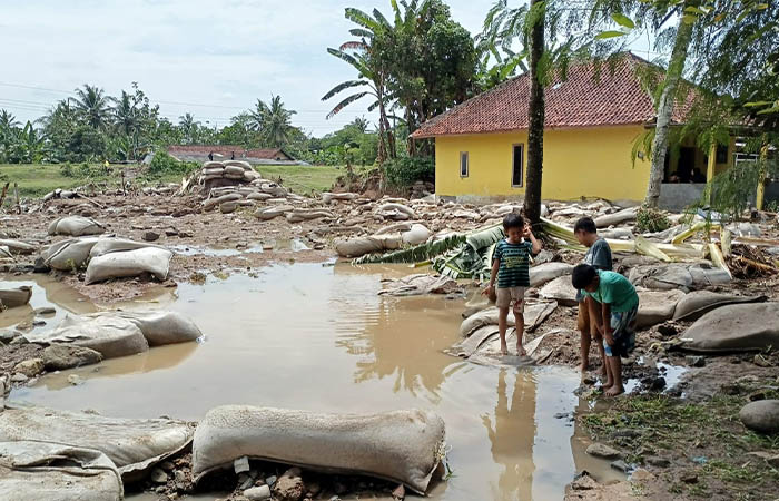 PORAK PORANDA: Anak kecil bermain di sekitar tanggul Sungai Karanganyar yang jebol, Minggu (9/11). Tumpukan karung berisi pasir yang dijadikan tanggul berserakan setelah tak mampu menahan arus sungai.