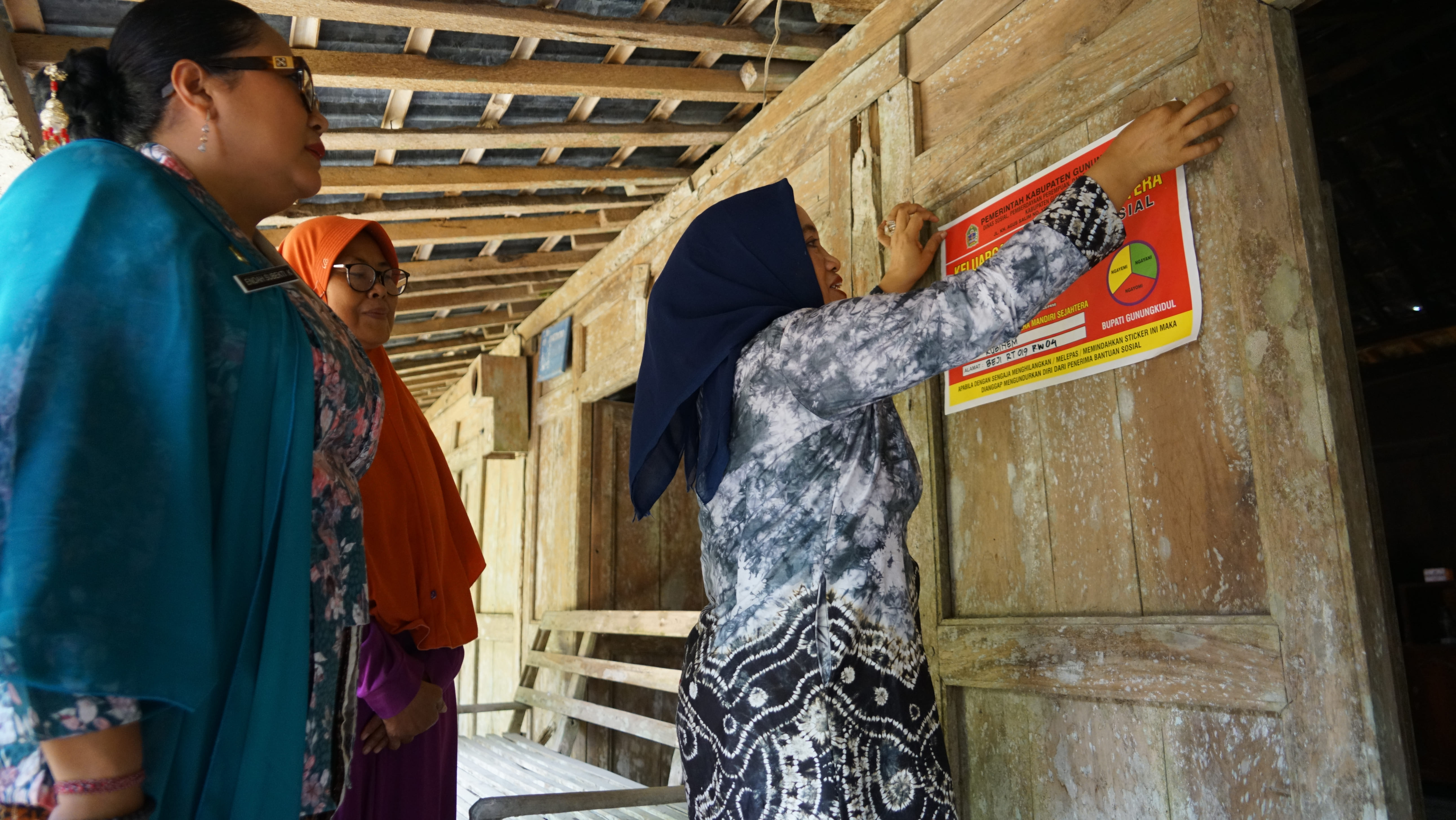 Bupati Gunungkidul Endah Subekti Kuntariningsih sedang menempelkan stiker kelurga miskin di dinding rumah warga Kalurahan Beji Kapanewon Patuk pada Kamis pagi (11/12).  &nbsp;