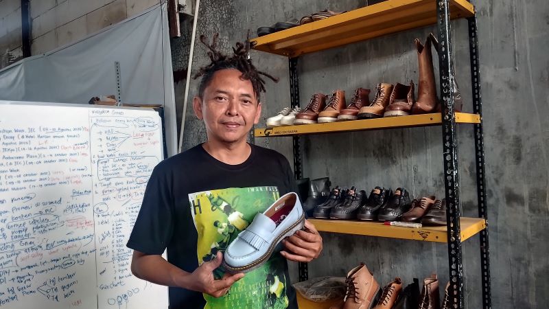 KARYANYA: Gondo sedang memegang sepatu yang diproduksinya Minggu (14/12).