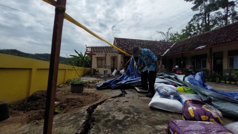RUSAK: Seorang guru menunjukkan halaman sekolah yang berada di perbukitan merekah, dampak hujan intensitas tinggi sejak akhir tahun lalu.